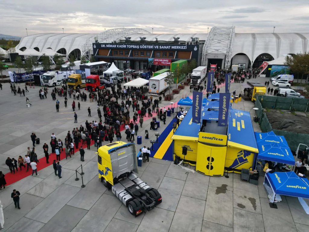 Crowded outdoor exhibition area at logitrans 2025 featuring branded stands and a truck on display near the main entrance.